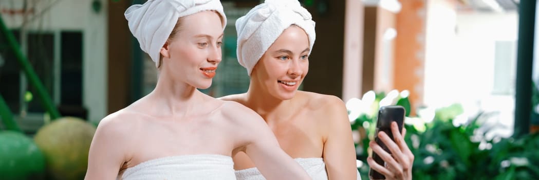 Couple of young beautiful women with beautiful skin in white towel taking a photo together at outdoor surrounded by peaceful natural environment. Beauty and healthy spa concept. Tranquility.