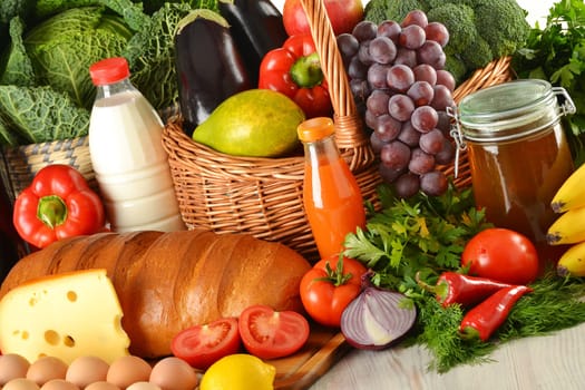 Groceries in wicker basket including vegetables, fruits, bakery and dairy products and wine isolated on white
