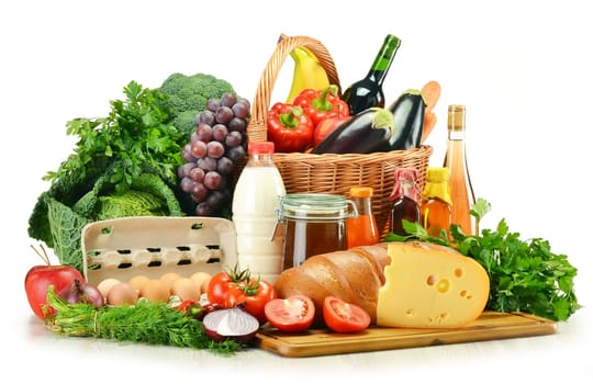 Groceries in wicker basket including vegetables, fruits, bakery and dairy products and wine isolated on white