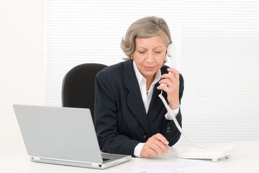 Serious successful senior businesswoman sitting behind office table portrait