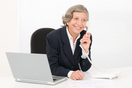 Smiling successful senior businesswoman sitting behind office table portrait