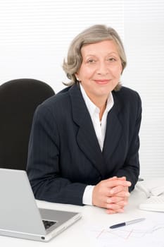 Successful senior businesswoman sitting behind office table with laptop portrait