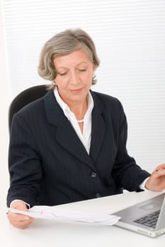 Successful senior businesswoman sitting behind office table with laptop portrait