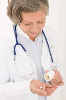 Medical doctor senior female holding pills looking down smiling portrait