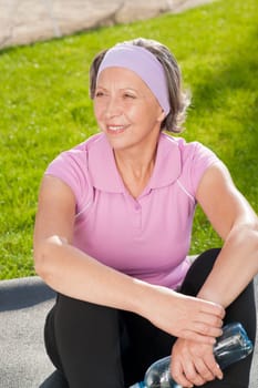 Senior sportive woman sitting on mat outside sunny day