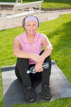 Senior sportive woman sitting on mat outside sunny day