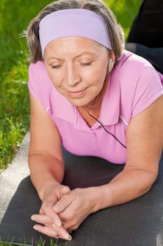 Senior sportive woman on mat listen music outside sunny day
