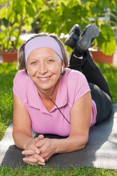 Senior sportive woman on mat listen music outside sunny day