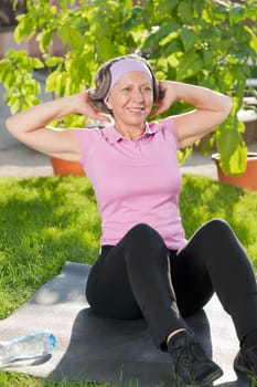 Senior sportive woman exercising on mat doing sit-ups sunny outdoor