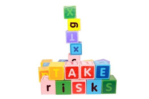assorted childrens toy letter building blocks against a white background that spell take risks
