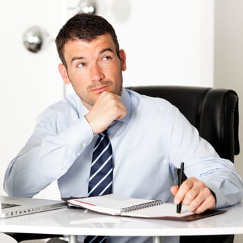 pensive businessman looking up in office with pen