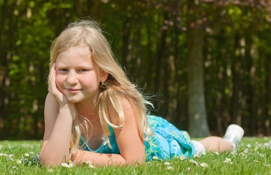 Blond teenager girl lying on the grass in a bright sunny day