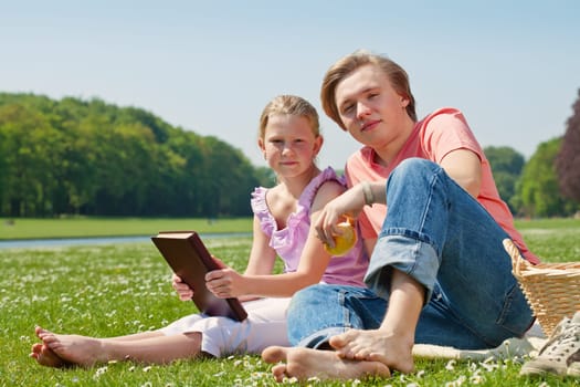 Teenager brother and sister having a picnic in the park in a bright sunny day