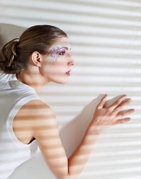 Pretty young woman lean lit by bright sunlight coming through the blinds