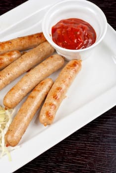Grilled sausages with cabbage, greens and tomato sauce on white plate