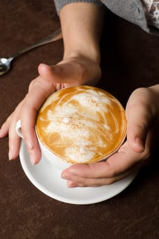 Closeup of female hands holding cup of Cappuccino