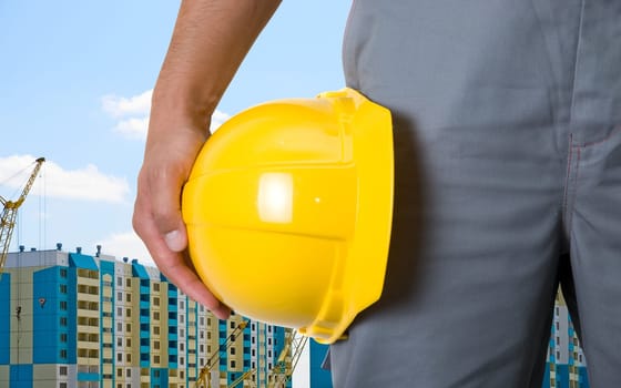 Closeup of yellow helmet at builder hands on building background