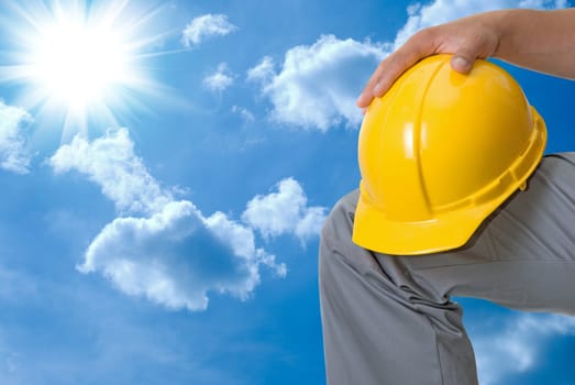 Closeup of yellow helmet at builder hands on blue sky background