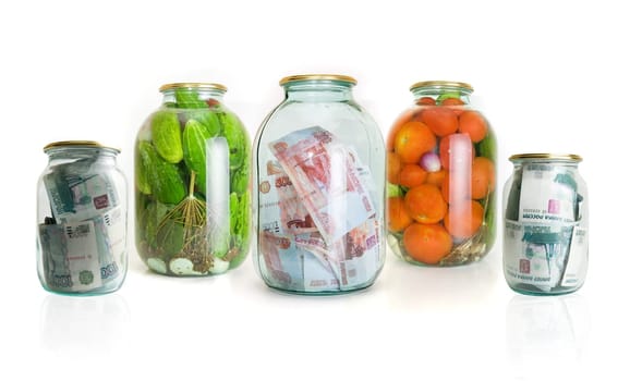 Glass jars with cucumbers tomatoes and money on a white background