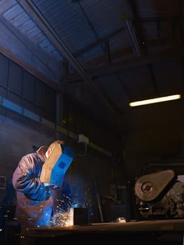 Manual worker in steel factory using welding mask, tools and machinery on metal. Vertical shape, side view, waist up