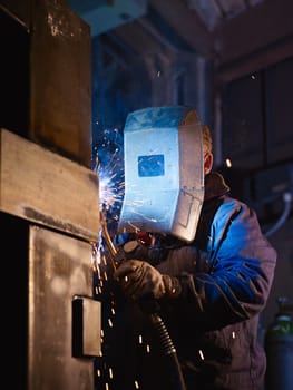 Manual worker in steel factory using welding mask, tools and machinery on metal. Vertical shape, side view, waist up