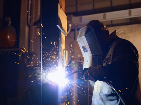 Manual worker in steel factory using welding mask, tools and machinery on metal. Horizontal shape, side view, waist up