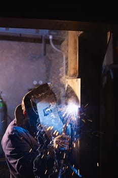Manual worker in steel factory using welding mask, tools and machinery on metal. Vertical shape, side view, copy space