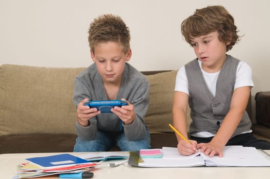 Two friends doing their homework in the livingroom. One of them is gaming, the other one is not ready and is jealous.