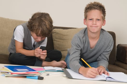 Two friends doing their homework in the livingroom. One of them is gaming, the other one is not ready and is jealous.