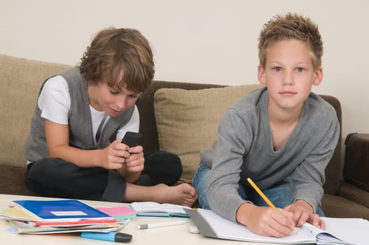 Two friends doing their homework in the livingroom. One of them is gaming, the other one is not ready and is jealous.