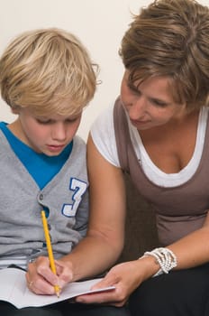 Boy is doing his homework in the livingroom while mother is helping him