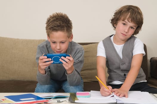 Two friends doing their homework in the livingroom. One of them is gaming, the other one is not ready and is jealous.