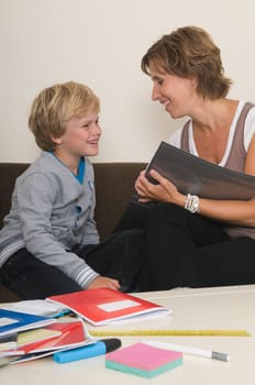 Boy is doing his homework in the livingroom while mother is helping him