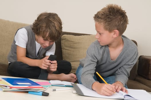 Two friends doing their homework in the livingroom. One of them is gaming, the other one is not ready and is jealous.