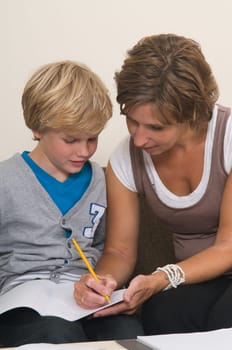 Boy is doing his homework in the livingroom while mother is helping him