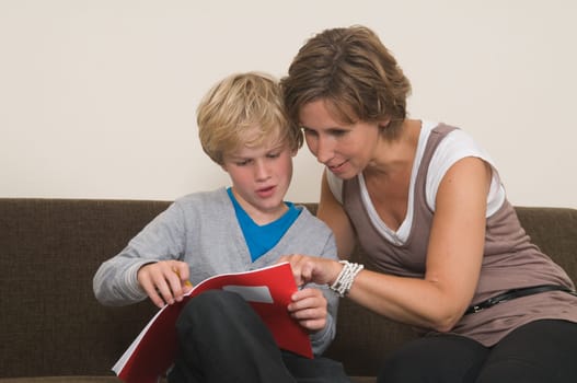 Boy is doing his homework in the livingroom while mother is helping him