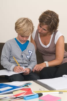 Boy is doing his homework in the livingroom while mother is helping him