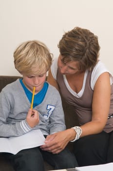 Boy is doing his homework in the livingroom while mother is helping him
