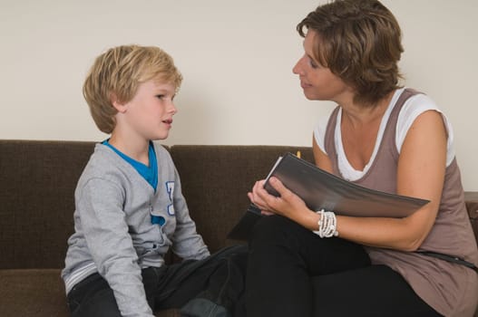 Boy is doing his homework in the livingroom while mother is helping him