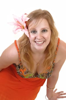 A beautiful blond teenager sitting on the floor, smiling into the camera with a pink lily in her hair and in a colorful orange dress, for white background.