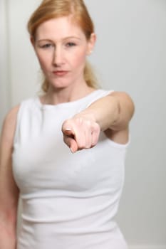 Young woman pointing resolutely towards the camera. It can be seen blurred in the background.