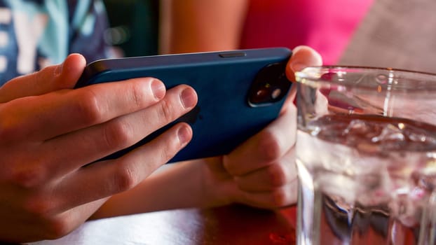 Mont-Tremblant QC Canada - 22.09.2024: Close-up of a person using a smartphone with a glass of water on the side.