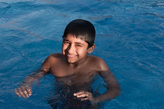 an handsome indian boy swimming happily in the pool