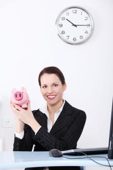 Pretty caucasian businesswoman holding piggy bank in the office.
