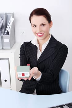 Beautiful caucasian businesswoman sitting in the office holding little house.