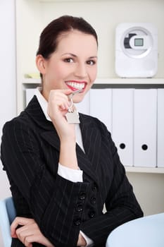 Pretty caucasian businesswoman sitting in the office holding keys.