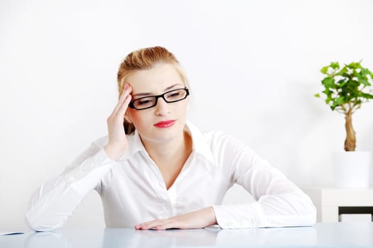 Middle-aged woman sitting behind the desk in the office having headache.