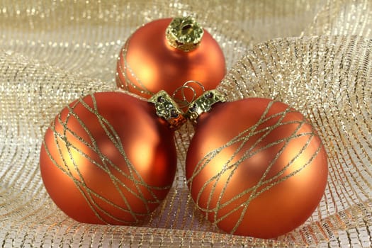three Christmas tree baubles on golden decorative fabric