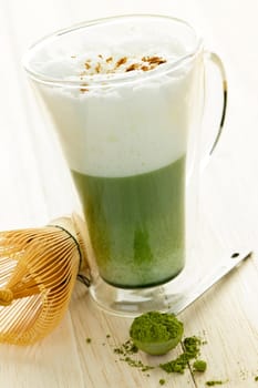 Matcha green tea latte beverage in glass mug with whisk