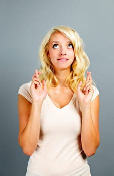 Blonde caucasian woman wishing with fingers crossed on gray background